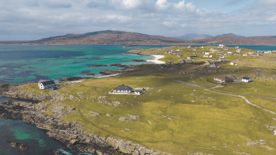 Aerial view of Outer Hebrides coastline, turquoise sea, white sand beach, green fields, and scattered homes.