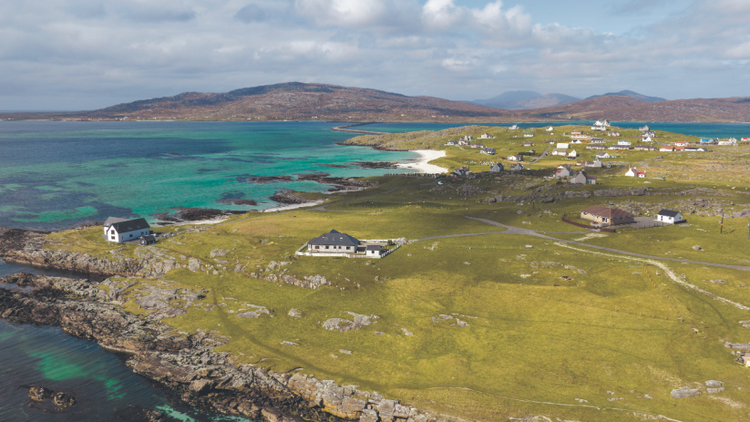 Aerial view of Outer Hebrides coastline, turquoise sea, white sand beach, green fields, and scattered homes.