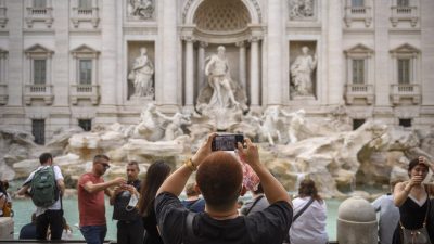 Tourists photograph the ornate white marble Trevi Fountain in Rome, Italy.