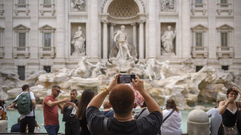 Tourists photograph the ornate white marble Trevi Fountain in Rome, Italy.