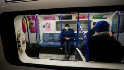 Passenger wearing a blue surgical mask and coat on a London Underground train.