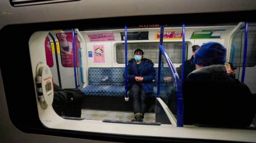 Passenger wearing a blue surgical mask and coat on a London Underground train.
