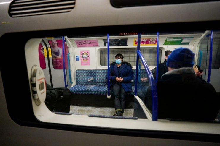Passenger wearing a blue surgical mask and coat on a London Underground train.