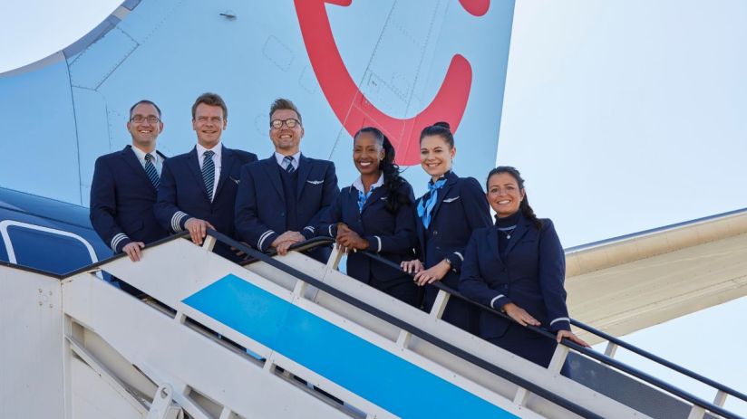 TUI airline crew, pilots and flight attendants, smiling on aircraft stairs with the TUI tail logo in the background