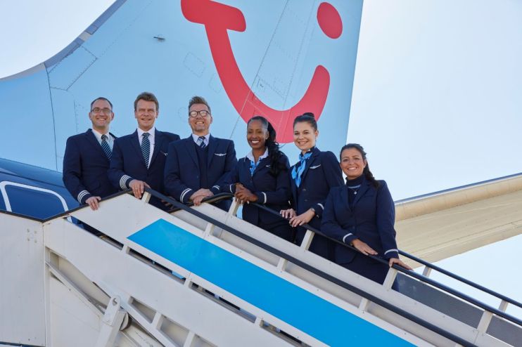 TUI airline crew, pilots and flight attendants, smiling on aircraft stairs with the TUI tail logo in the background