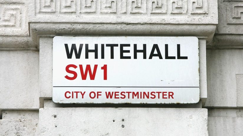 Whitehall SW1 street sign in the City of Westminster, London, mounted on a white stone wall with decorative trim.