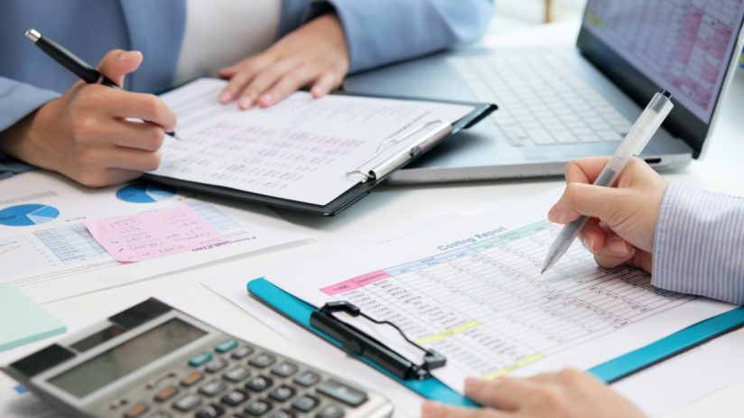Two business professionals review and analyze a costing report with a calculator and laptop on a desk.