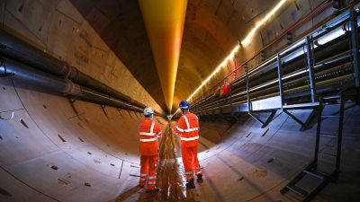 Two engineers in hard hats and high-visibility gear inspecting a large, illuminated tunnel under construction.