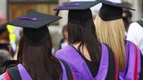 Three graduates in black caps with purple tassels and purple academic gowns from behind.