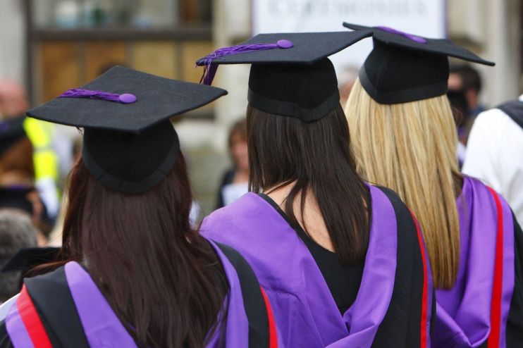 Three graduates in black caps with purple tassels and purple academic gowns from behind.