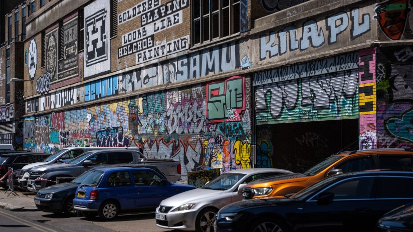 Vibrant graffiti art covering a brick building with parked cars in front, Truman Brewery area.