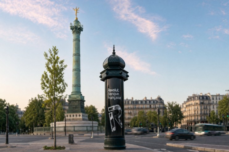 Revolut Banque Fran&ccedil;aise ad on a Morris column in Paris, with the July Column and blurred traffic in the background.