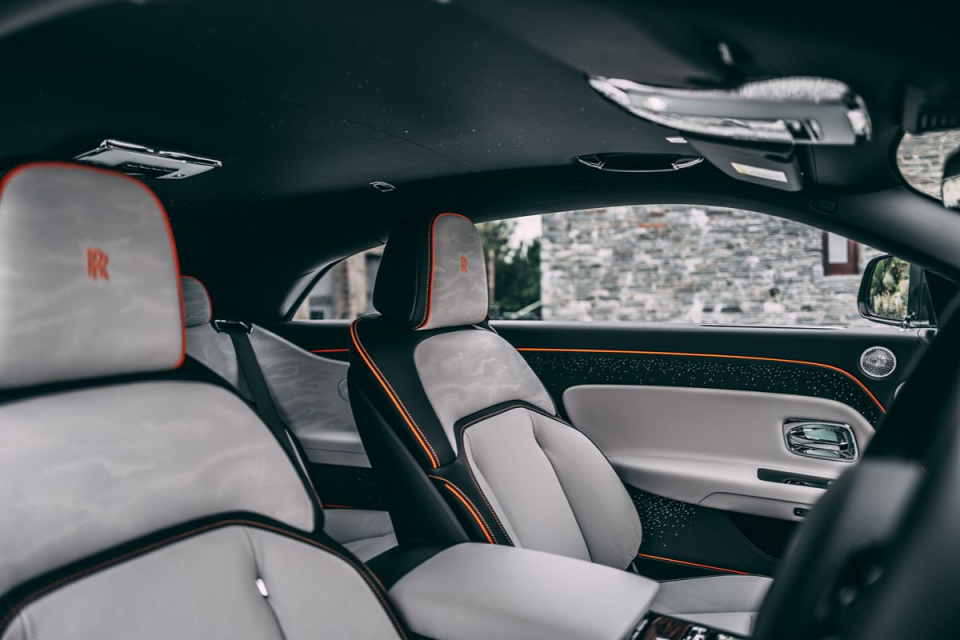 Luxurious car interior with custom light grey and black seats, orange piping, and illuminated door panel details