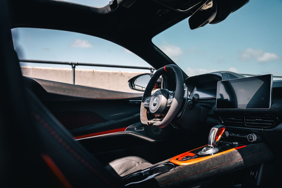 Modern car interior with black leather, orange accents, steering wheel, digital display, and gear selector.