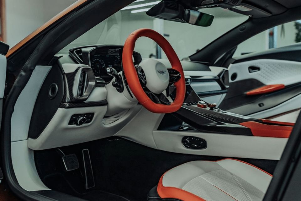 Luxury car interior with white and orange seats, red steering wheel, and carbon fiber dashboard accents