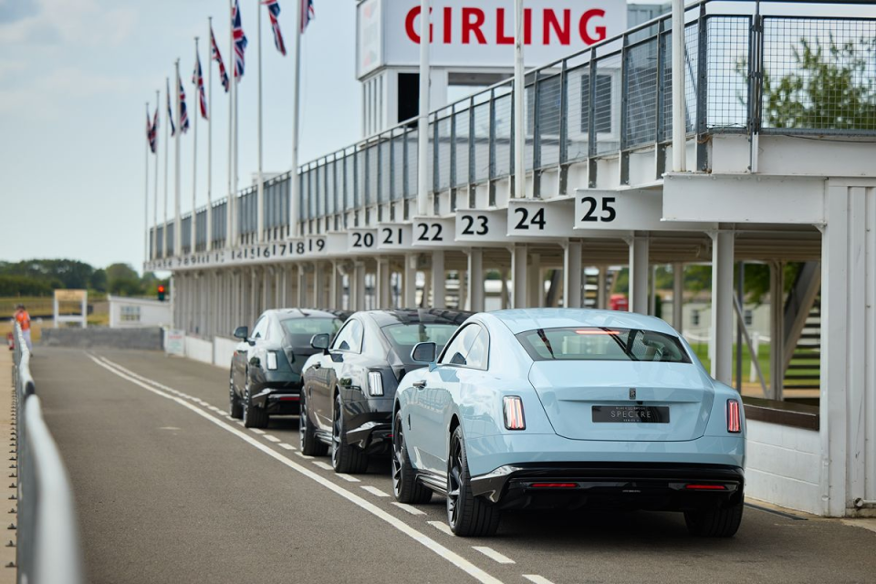 Three Rolls-Royce Spectre electric vehicles lined up on a racetrack with the Girling pit lane building in the background.