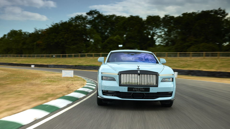 Light blue Rolls-Royce Spectre electric car on a racetrack, with a blurred green landscape in the background.