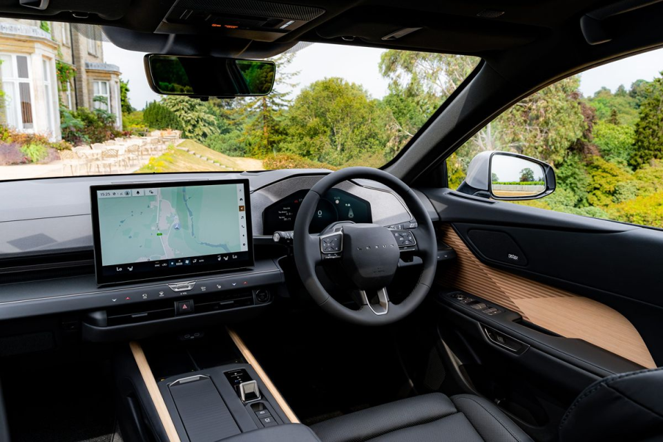Interior view of a modern car dashboard with a large touchscreen navigation display, steering wheel, and luxurious wood trim.
