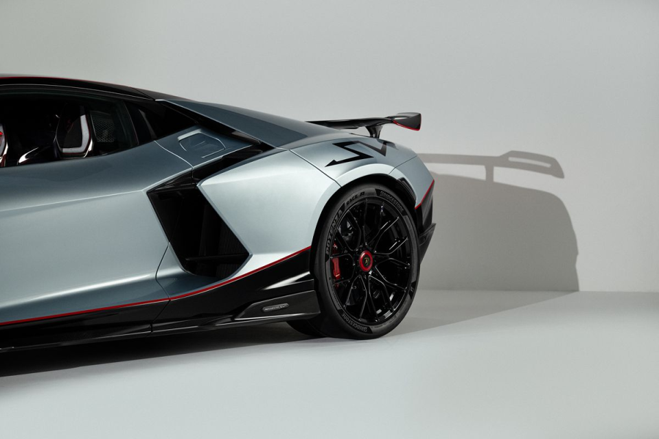 Rear quarter view of a silver Lamborghini Aventador with black wheels, red trim, and a rear spoiler