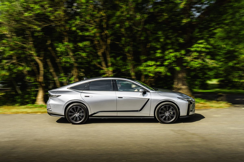 Sleek silver sedan driving on a road with blurred green trees in the background, conveying motion.