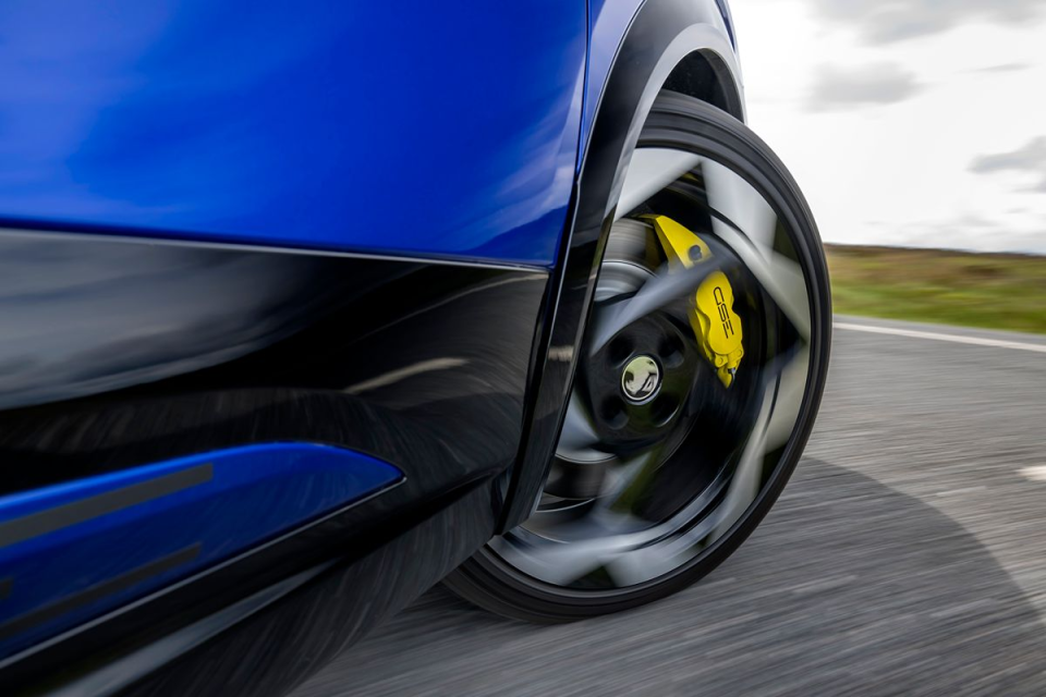 Close-up of a blue cars spinning wheel with bright yellow brake calipers, blurring motion on a road