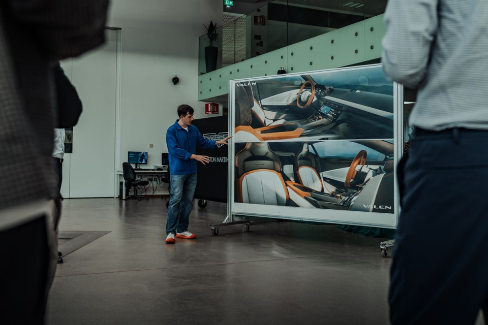 Man in blue shirt presenting car interior designs on a large display board in a modern office.