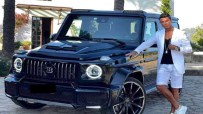 Cristiano Ronaldo in a white suit and shorts, leaning on a black Brabus G-Wagon luxury SUV.