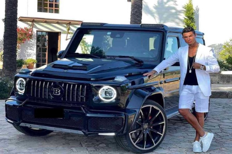 Cristiano Ronaldo in a white suit and shorts, leaning on a black Brabus G-Wagon luxury SUV.