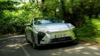 Silver Lexus ES driving on a tree-lined road, motion blur implying speed, front view, lush green foliage