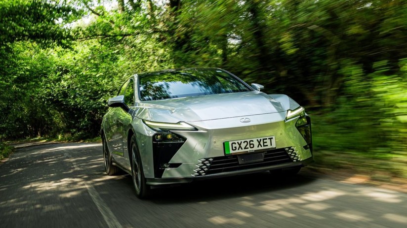 Silver Lexus ES driving on a tree-lined road, motion blur implying speed, front view, lush green foliage