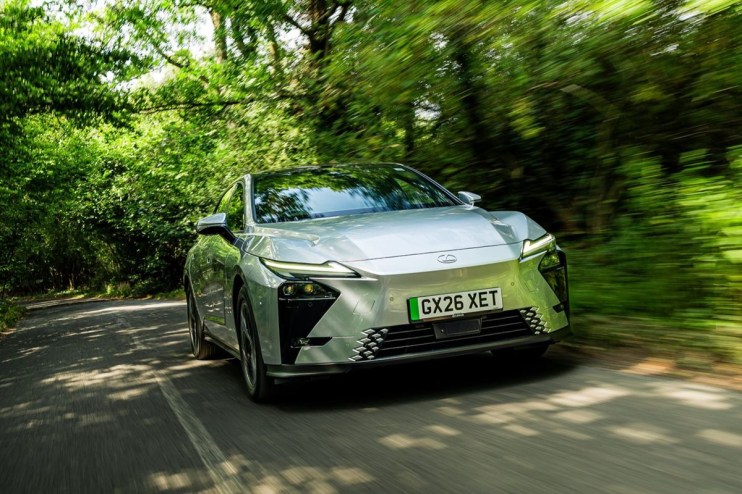 Silver Lexus ES driving on a tree-lined road, motion blur implying speed, front view, lush green foliage