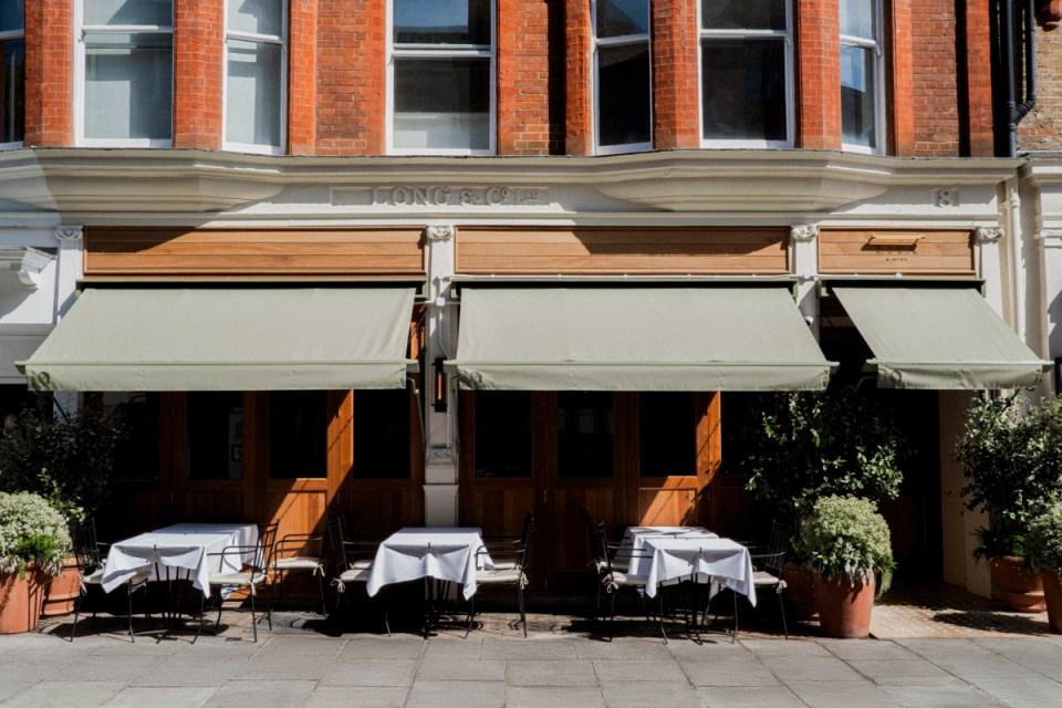 Exterior of Long & Co. restaurant with green awnings, outdoor dining tables, and potted plants on a sunny day.
