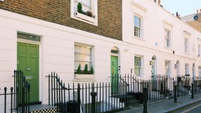 Row of classic London terraced houses with white facades and green doors, indicating UK property.