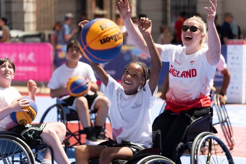 Joyful children in wheelchairs playing basketball with an instructor at a London sports festival session.