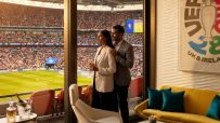 Couple in a luxury stadium suite enjoying a soccer match, with food, drinks, and a UEFA poster.
