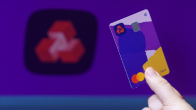 Hand holding a NatWest debit card with a colorful design, blurred NatWest logo in the background.