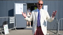 Nigel Farage, in a striped jacket and sunglasses, speaks outside a polling station.