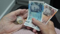Elderly hands holding British pound notes (&pound;5, &pound;10) and coins, representing pension funds and finances.