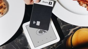 Hand holding black SumUp payment card over a white contactless reader on a marble table with breakfast food