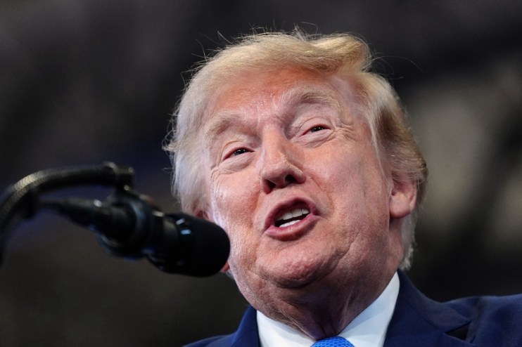 Donald Trump speaking at a podium, microphone visible, discussing the Strait of Hormuz