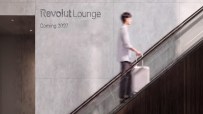 Revolut Lounge sign on a concrete wall with a person on an escalator holding a rolling suitcase.