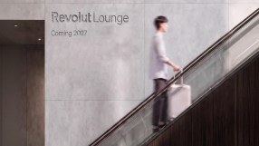 Revolut Lounge sign on a concrete wall with a person on an escalator holding a rolling suitcase.