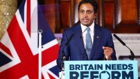 Zia Yusuf speaking at a Reform UK press conference, with a Union Jack flag and Britain Needs Reform sign.