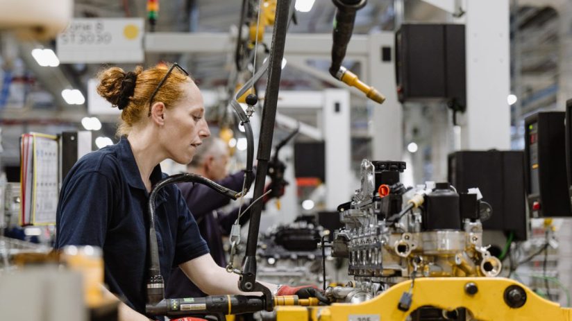 Female factory worker in red gloves assembling machinery on an industrial production line.