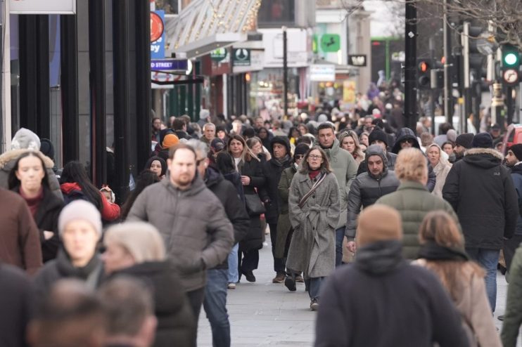 Crowd of people walking on a busy city street with shops and traffic lights in the background