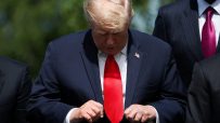 Donald Trump adjusts his suit and red tie, with an American flag pin visible on his lapel.