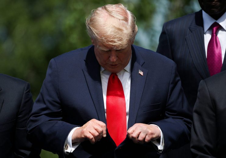 Donald Trump adjusts his suit and red tie, with an American flag pin visible on his lapel.