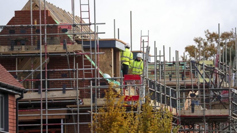 Construction workers in hard hats and high-visibility jackets on scaffolding at a new build house site