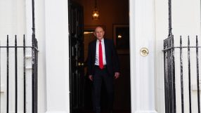 A man in a dark suit and red tie walks through a doorway with black iron railings on either side.