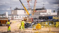 Construction site with two workers, cranes, building materials, and a building under construction.